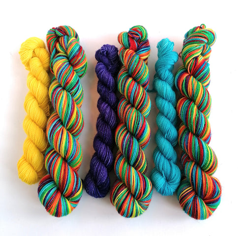 Rainbow sparkle sock yarn sets on a white background.  3 50g variegated skiens, each with a semi-solid mini skein - one in yellow, one in purple, one in turquoise. 