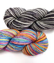 Load image into Gallery viewer, Two skeins of yarn on a white background: one black and white variegated, and one bright rainbow multicolor variegated.
