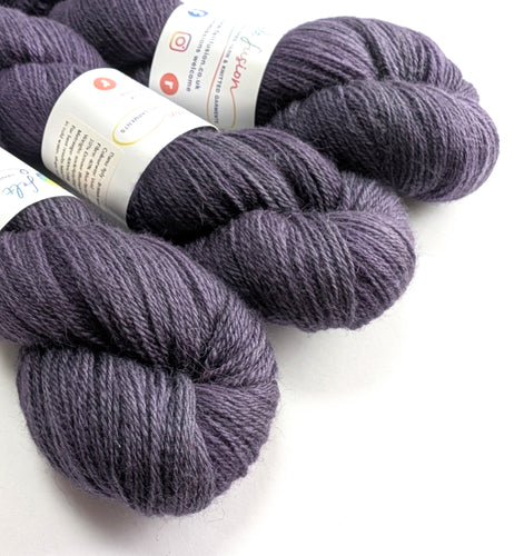 Three skeins of purple yarn with labels on a white background
