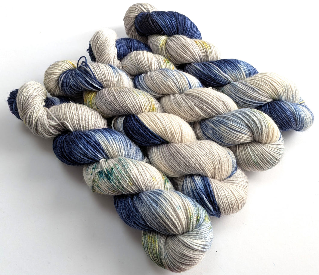 Four skeins of navy blue and silver grey yarn with speckles. 

