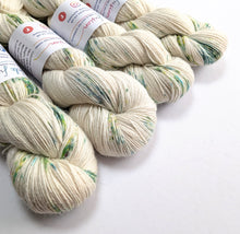 Load image into Gallery viewer, Four skeins of cream-colored yarn with green and blue speckles on a white background.
