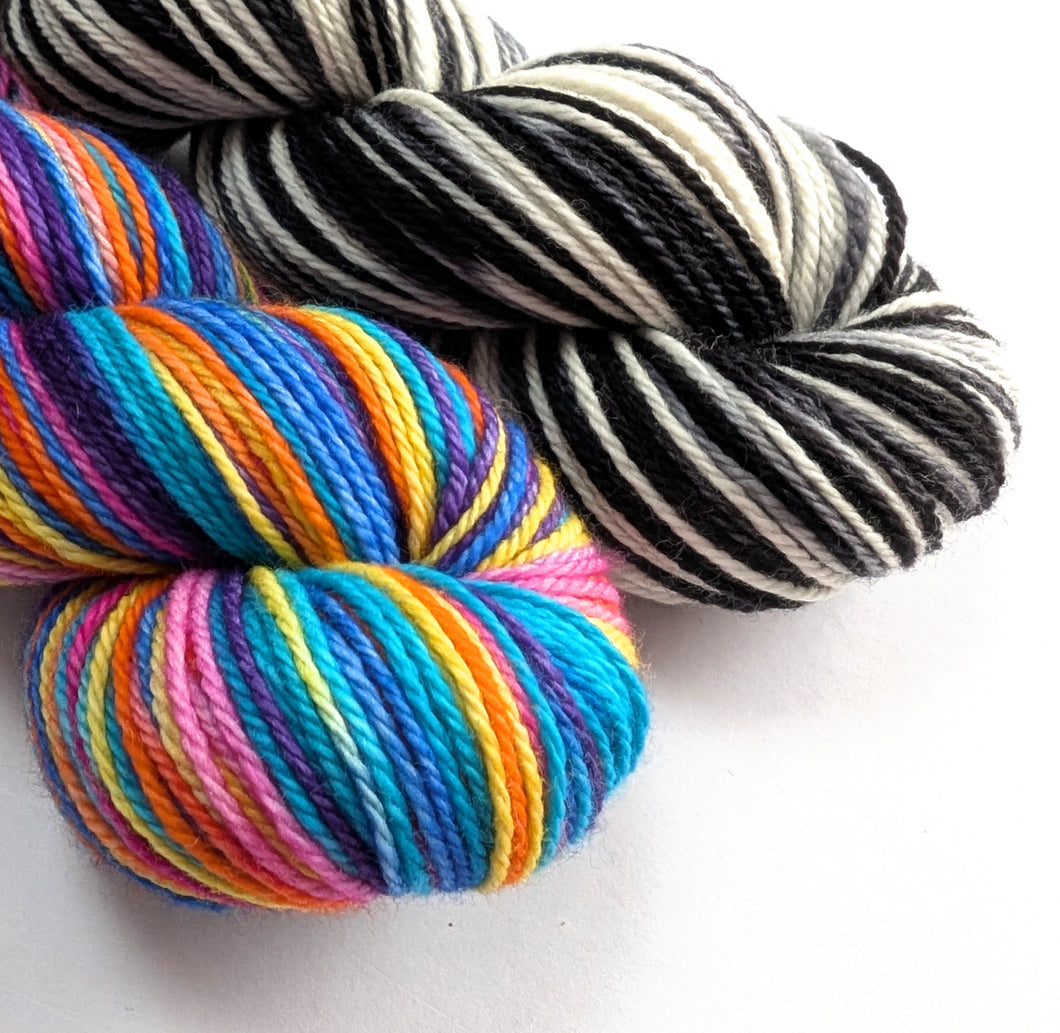 Two skeins of yarn, one multicolored and one black and white striped, on a white background.