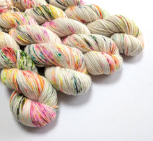 Load image into Gallery viewer, A pile of hanks of variegated yarn on a white background. The yarn is primarily a warm off-white/cream base with scattered multicolored flecks in pink, orange, yellow, green, and blue.
