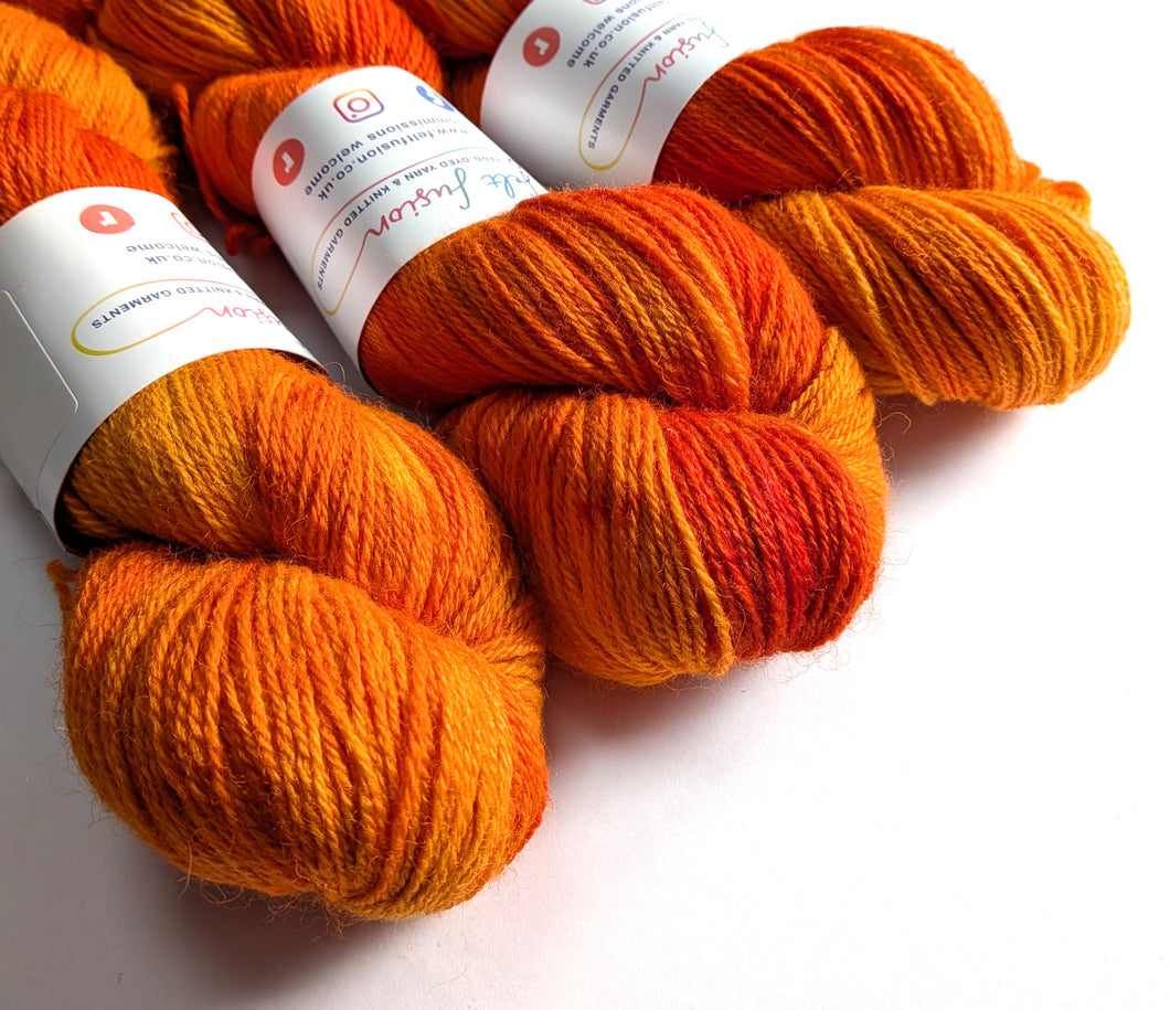 Three skeins of orange yarn with labels on a white background