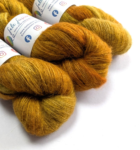 Three skeins of gold and yellow yarn with labels on a white background
