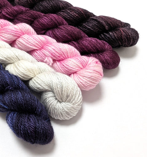 Five skeins of yarn in various colors on a white background