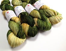 Load image into Gallery viewer, Four skeins of variegated yarn with white paper labels, showing a color-shifting pattern of deep forest green, olive, and pale yellow, arranged on a plain white background.
