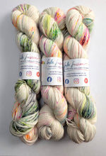 Load image into Gallery viewer, Three skeins of multicolored yarn with visible branding on a light gray background
