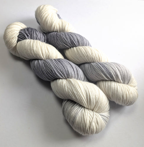 Two skeins of grey and white yarn on a light gray background