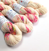 Load image into Gallery viewer, Several skeins of variegated yarn arranged on a white background. The yarn is a warm cream/off-white color with colorful variegated flecks in pink, green, and blue.
