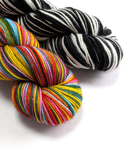 Two skeins of yarn, one multicolored and one black and white striped, on a white background.