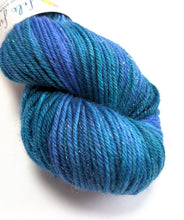 Load image into Gallery viewer, A skein of variegated yarn in shades of teal, blue, and purple, with a white paper label partially visible at the top, set against a plain white background.
