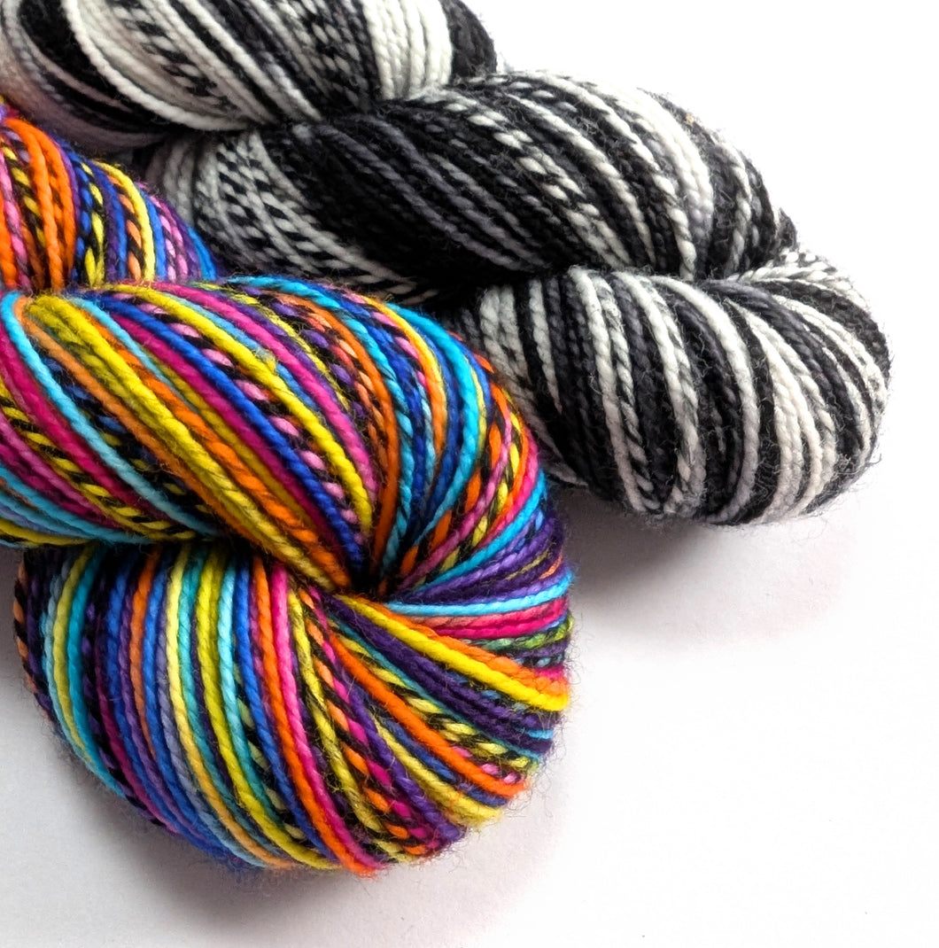 Two skeins of yarn, one multicolored and one black and white striped, on a white background.