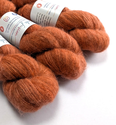 Three skeins of orange yarn with labels on a white background