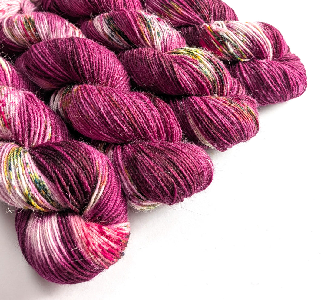 Skeins of pink and purple yarn with speckles on a white background