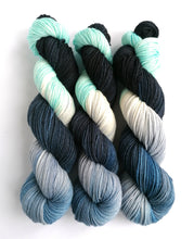 Load image into Gallery viewer, 3 skeins of yarn, dyed in light blue, shades of navy and black, with undyed/white areas. 
