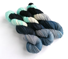 Load image into Gallery viewer, 3 skeins of yarn, dyed in light blue, shades of navy and black, with undyed/white areas.
