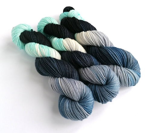 3 skeins of yarn, dyed in light blue, shades of navy and black, with undyed/white areas.