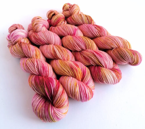 4 twisted skeins of yarn dyed in pink, with pink and gold and olive green splashes, on a white background.