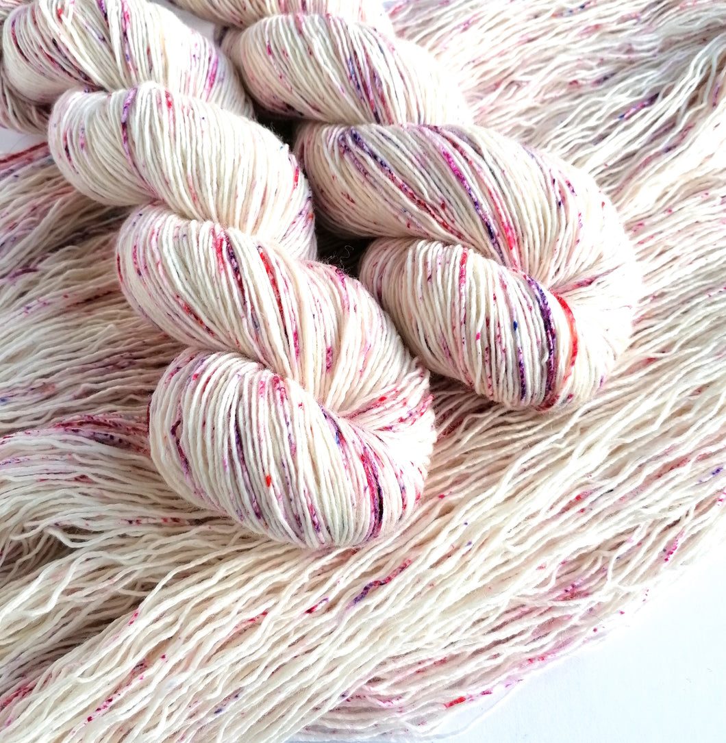 2 twist skeins of natural yarn, with pink, red and purple speckles, laying on opened out skeins.